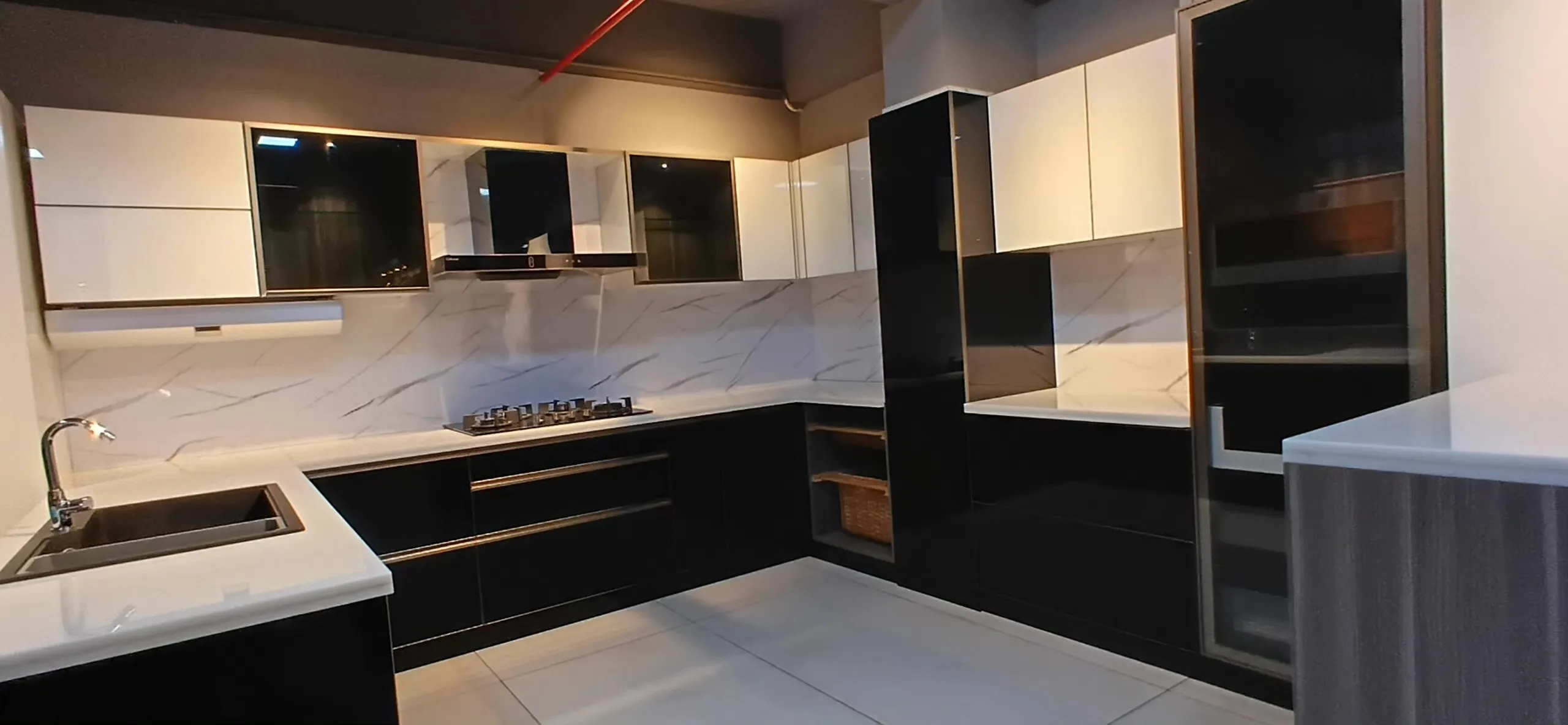 A display kitchen at the Pankaj Interiors showroom, with black gloss cabinetry, a marble backsplash, a built-in hob and a wall-mounted chimney